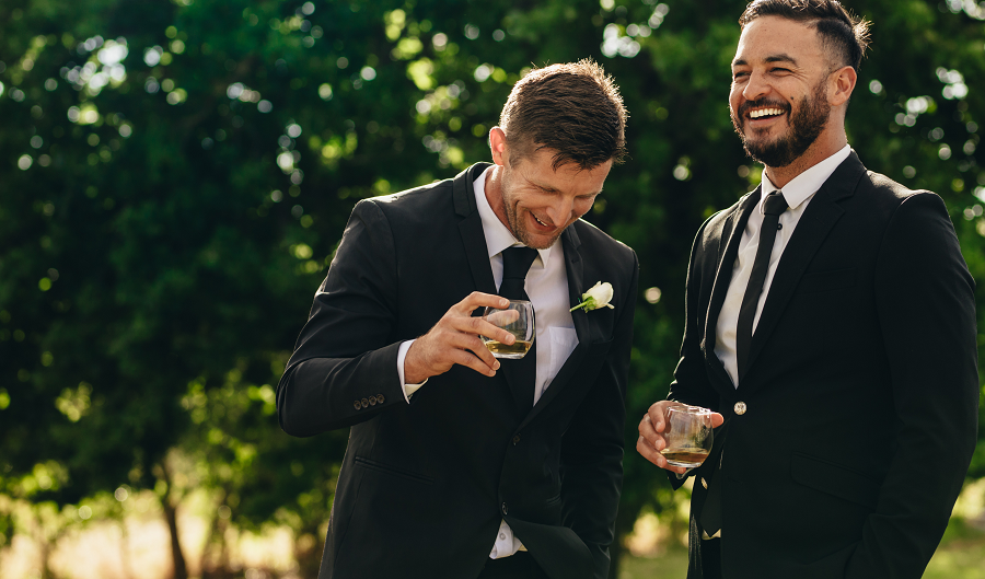 Two men in suits talking and laughing at a wedding.